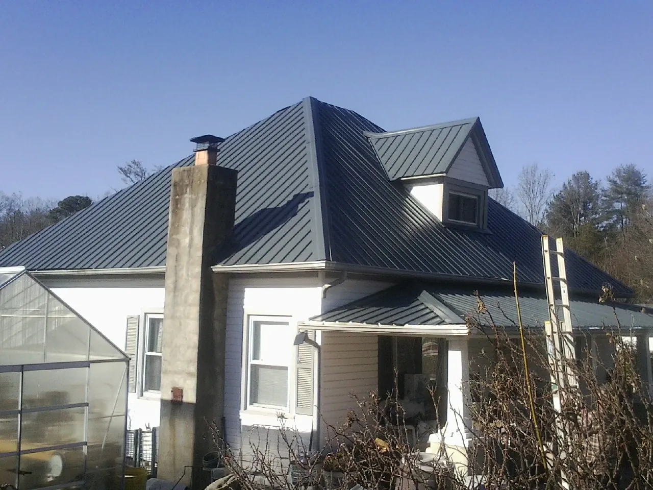 Dark blue standing seam metal roof on a white farmhouse with dormer — Slate & Tile Roof Repair by Roofing Brothers in Corona Del Mar