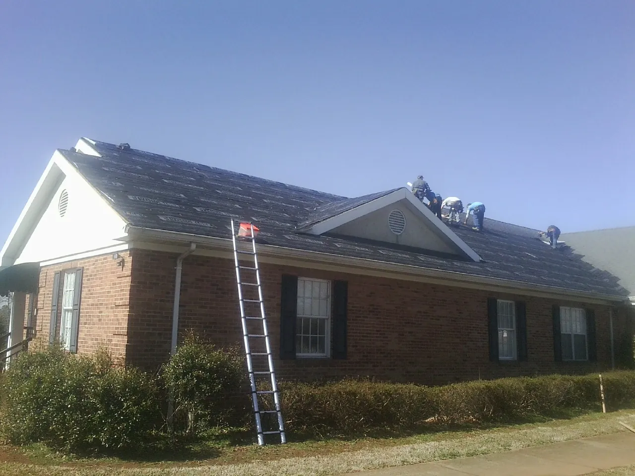 Crew tearing shingles off a brick ranch roof with a ladder set — Emergency Roof Repair work by our crew in Corona Del Mar