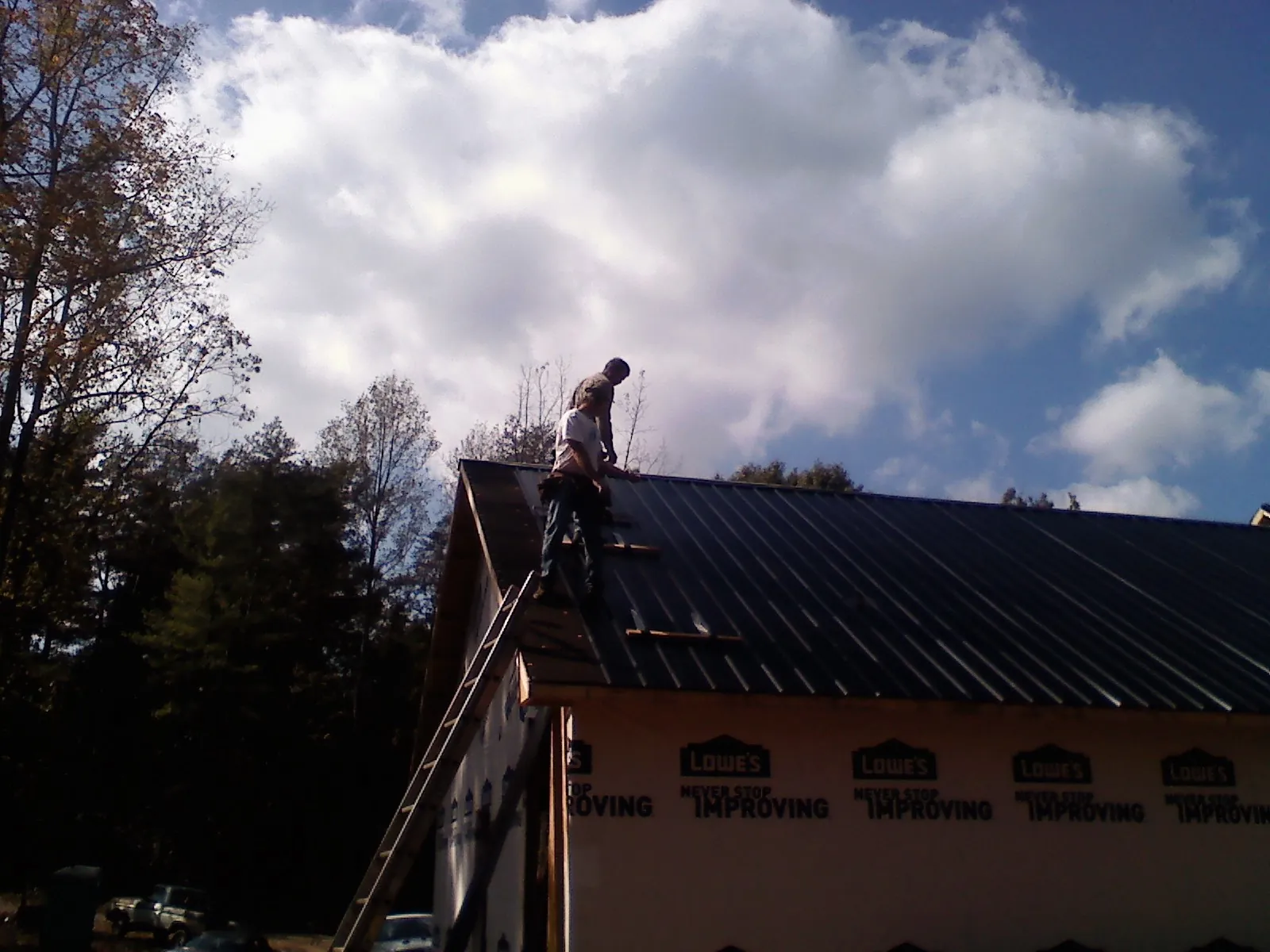 Roofer fastening dark metal panels high against a cloudy sky, from a Roof Inspection job in Corona Del Mar