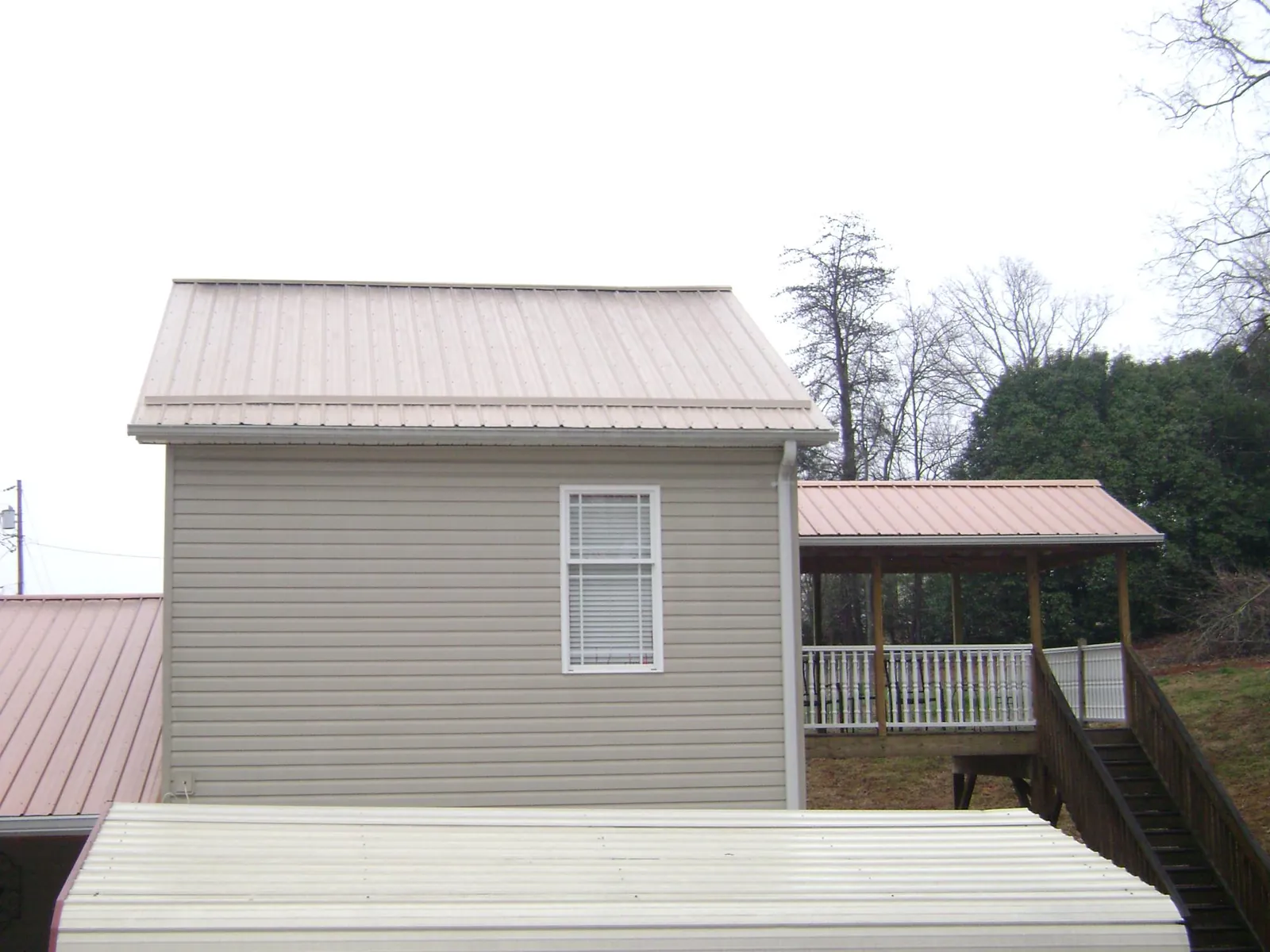 Tan metal roofs on a two story addition and attached porch, from a Roof Replacement job in Corona Del Mar